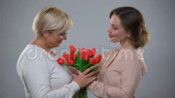 年轻的女性带着郁金香和拥抱爱和关怀向年长的母亲展示视频的预览图