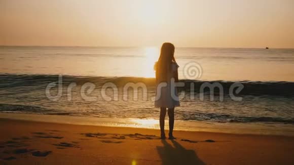 我的后景拍摄快乐的小女孩观看不可思议的日落在史诗般的金色海洋海滩触摸温暖的波浪视频的预览图
