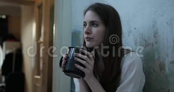 一个女人一位黑发长发的年轻女子坐在地板上怀里抱着一个杯子躺在室内的一个黑暗的房间里视频的预览图