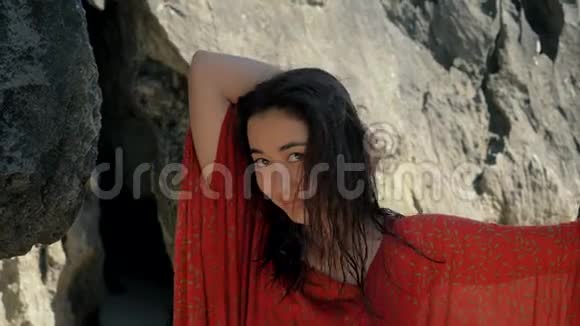 年轻漂亮的女孩穿着红色的裙子站在岩石之间看着相机造型美观视频的预览图