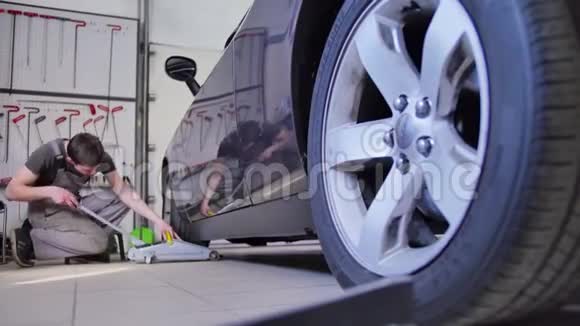 男主人用千斤顶举起汽车的车轮以便在汽车修理店修理工具凹痕对齐伙计视频的预览图