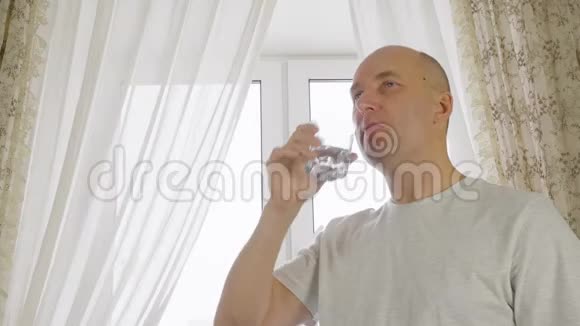 家厨房窗户背景玻璃上的成年秃头男子饮用水视频的预览图