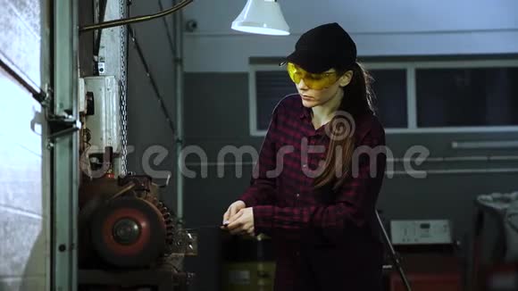 漂亮的女孩穿着格子衬衫黑色帽子和护目镜在磨床上工作从事男性职业的妇女视频的预览图