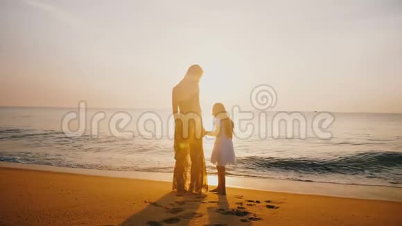 惊人的后景拍摄快乐的母亲亲吻小女儿和牵手在史诗般的金色日落海滩视频的预览图