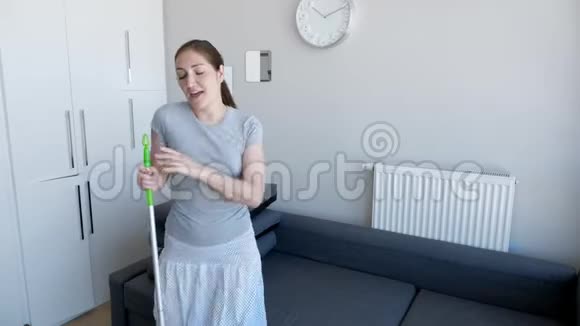 快乐的女人正在用拖把洗地板在她的现代公寓里唱歌跳舞视频的预览图