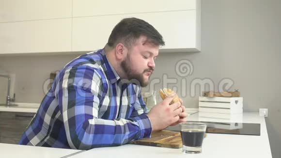 穿格子衬衫留着胡子的胖子吃快餐芝士汉堡用有害的柠檬水冲洗额外的卡路里视频的预览图