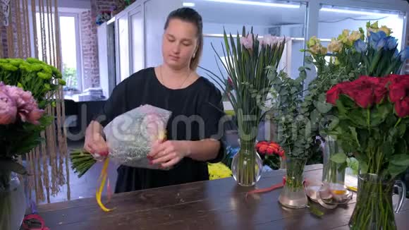 女子花店正在用白纸包装玫瑰花束视频的预览图