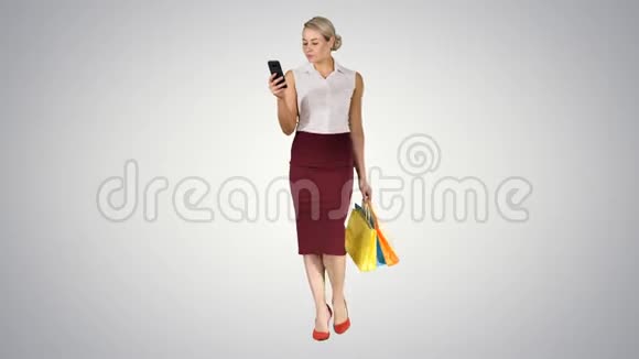 美丽迷人的女人看着智能手机拿着购物袋而走在梯度背景视频的预览图