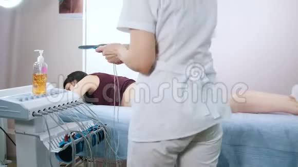 美容诊所年轻女子在床上打肌刺激一位医生把设备视频的预览图