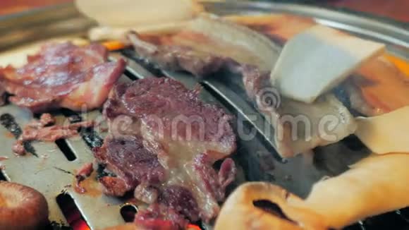 餐厅提供韩式烧烤特写一片培根和蘑菇炒在热烤架上视频的预览图
