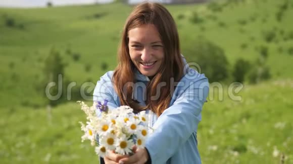 年轻快乐的女人在田野里捧着一束野花美丽的女人嗅嗅向前伸展花朵视频的预览图