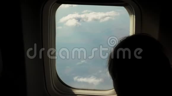特写从飞机窗户向外看天空云层和下面的风景的女孩的黑色剪影视频的预览图