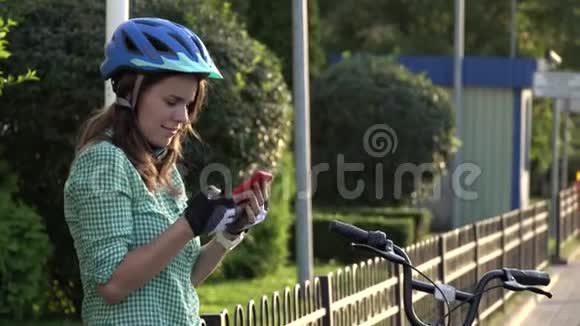 年轻的白种人女学生用手拿手机触摸屏幕一个女人站在阳光明媚的出租城市自行车附近视频的预览图