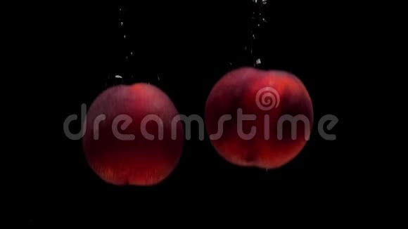 两个成熟的桃子在黑色的背景下落入透明的水中视频的预览图