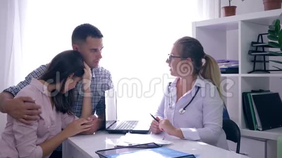医生对女人的健康有坏消息男人抱着妻子坐在医院的办公室里视频的预览图