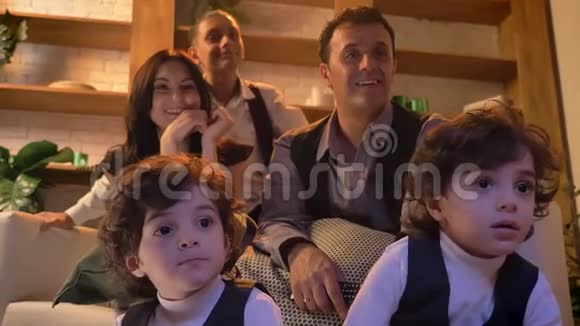两对可爱的阿拉伯卷发双胞胎正坐在客厅的地板上和家人一起仔细看电视视频的预览图
