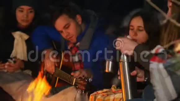 一群朋友在树林里的火边玩得很开心吃点心一个年轻人在弹吉他视频的预览图