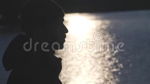 一位留胡子的年轻人在市中心一个蓝色湖泊中太阳反射的背景上的剪影视频的预览图