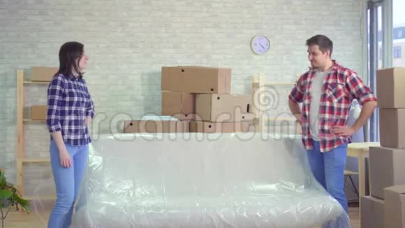 年轻的夫妇搬家后把油布从沙发上取下来视频的预览图