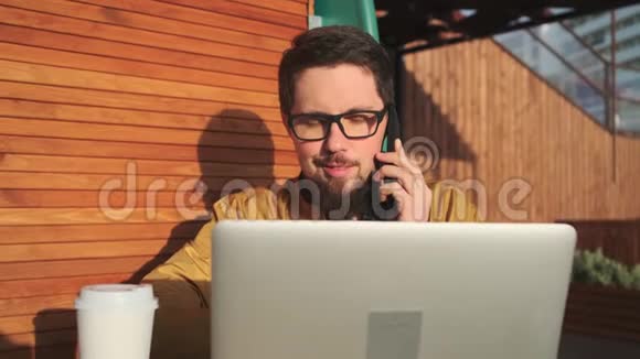 男人用手机说话看着笔记本坐在户外视频的预览图