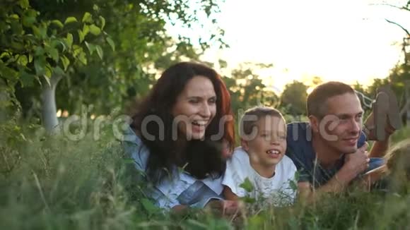 夫妻和三个孩子在日落时分躺在草地上暑假快乐的孩子和他们的父母视频的预览图