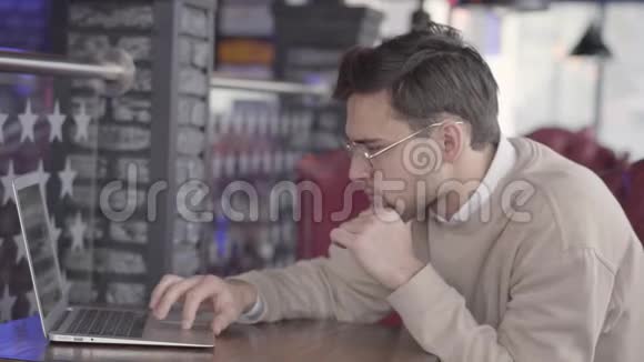 英俊的男人坐在咖啡馆里等待他的命令或在中心专心地在电脑上工作视频的预览图