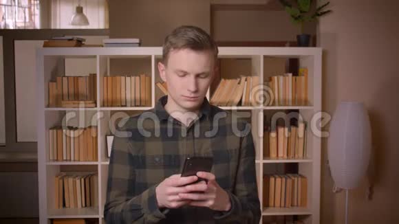 在大学图书馆里用电话拍摄年轻迷人的白种人男学生的特写镜头视频的预览图