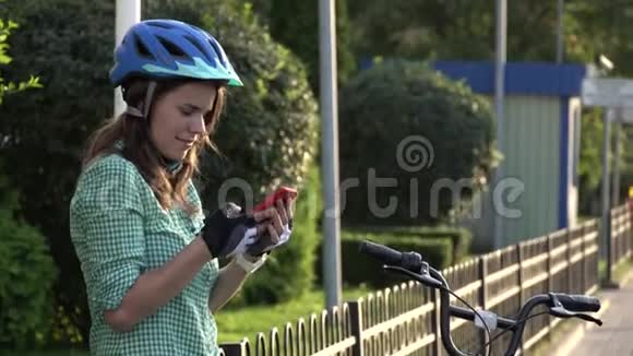 年轻的白种人女学生用手拿手机触摸屏幕一个女人站在阳光明媚的出租城市自行车附近视频的预览图