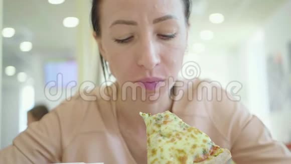一个年轻的女人正在吃一块披萨可爱的快乐女孩笑着咬着一大片新鲜披萨视频的预览图