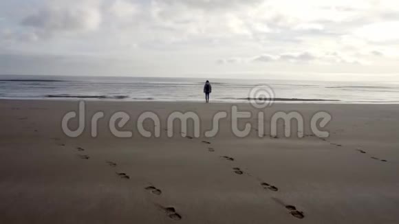 穿着衣服的女人站在海滩海滨沿着海岸线移动视频的预览图