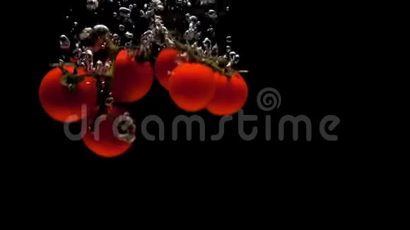 樱桃番茄的两个枝条在黑色的背景下落入透明的水中视频的预览图