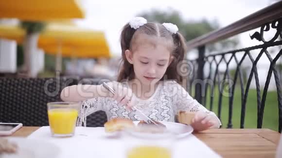 一个吃午饭的小女孩的肖像小女孩在街头咖啡馆里学着用刀叉吃饭视频的预览图