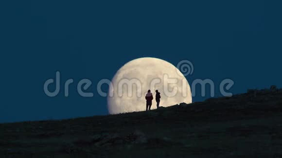 女人和孩子站在巨大的月亮背景下的剪影视频的预览图