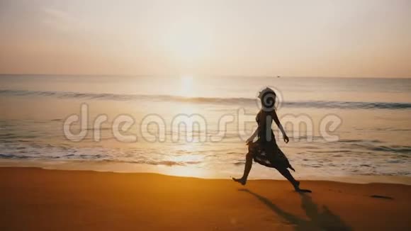 年轻美丽的快乐女人张开双臂沿着令人难以置信的金色夕阳海滩享受自由的时刻视频的预览图
