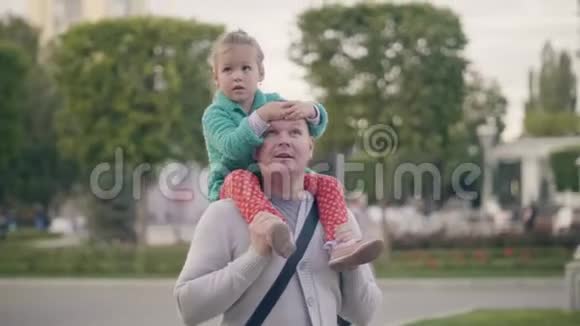年轻的爸爸在夏天公园骑着女儿的肩膀家庭周末快乐视频的预览图