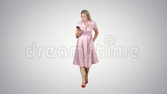 穿着粉色衣服的年轻女性看着移动智能手机在渐变背景下行走时发短信视频的预览图