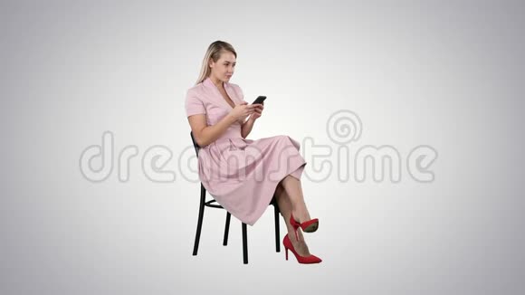 体贴的女人穿着粉色连衣裙在渐变背景下用智能手机发短信视频的预览图