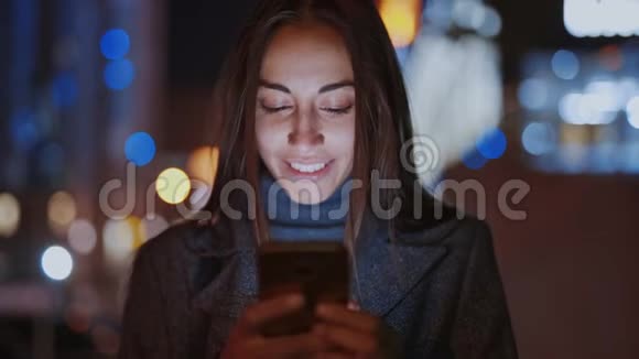 使用智能手机在夜间城市散步的漂亮微笑女人特写视频的预览图