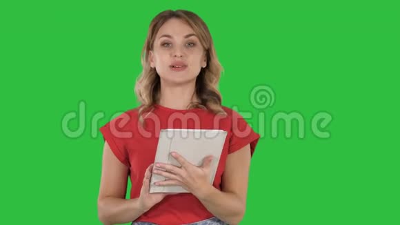 金发女人穿着红色的拿着平板电脑在绿色屏幕上阅读到相机Chroma键视频的预览图