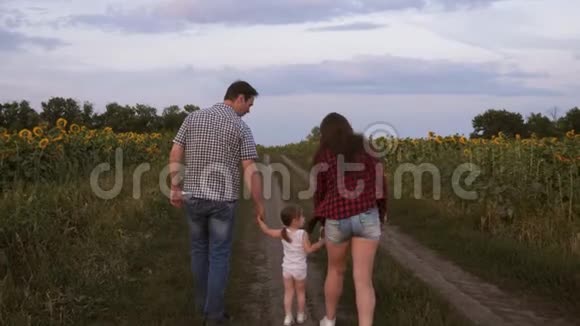 小女儿跳着手牵着爸爸妈妈一家人带着小孩走在路上在田野旁欢笑视频的预览图