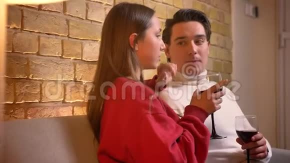 一对年轻的白种人夫妇在舒适的家中坐在沙发上喝着葡萄酒的侧写特写视频的预览图