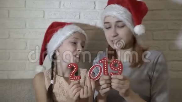 圣诞老人帽子里的两个姐姐手里拿着2019年的红色数字和她们一起玩耍跳舞微笑着坐着视频的预览图