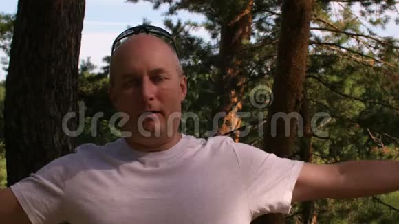 穿着白色t恤的快乐秃头在夏季森林或公园放松视频的预览图