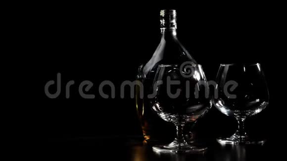 豪华白兰地圆瓶的金色干邑和两个玻璃杯旋转在一张木桌上玻璃在灯光下眩光白兰地白兰地视频的预览图