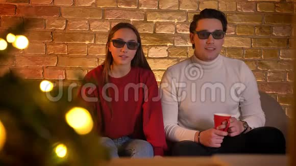 一对戴着3D眼镜的白种人夫妇坐在沙发上喝着一杯饮料看电影在圣诞节时感到震惊视频的预览图