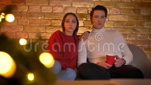 拥抱白种人夫妇坐在沙发上在圣诞节的气氛中用心看电影喝一杯饮料视频的预览图
