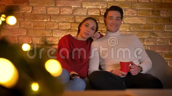 微笑着拥抱白种人夫妇坐在沙发上在电视上选择电影在舒适的家里喝杯饮料视频的预览图