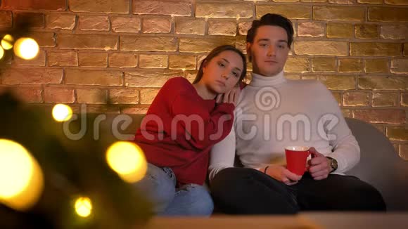 在舒适的家里一对白种人夫妇坐在沙发上一边喝着饮料一边看电影视频的预览图
