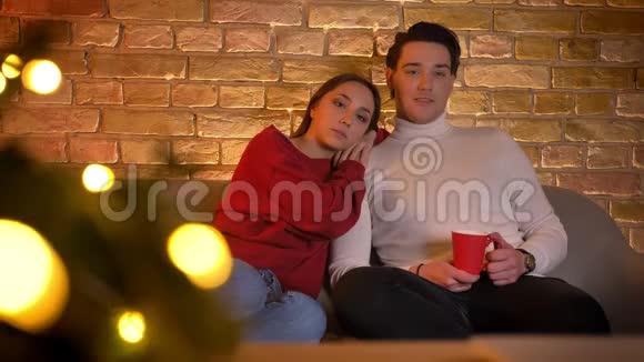 笑着拥抱白种人夫妇坐在沙发上在舒适的家庭氛围中喝着一杯饮料看电影视频的预览图