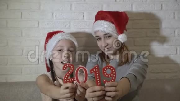 两个姐姐一个小女孩和一个十几岁的孩子戴着圣诞老人帽子戴着红色的数字玩着坐在上面微笑视频的预览图
